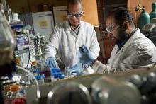 Dr. Edgardo standing next to a chemistry student in a lab doing experiments 